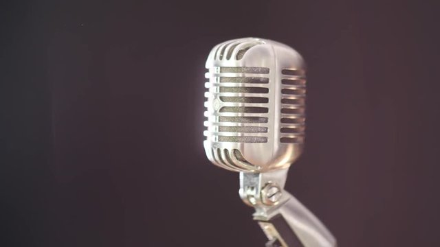 A vintage elvis microphone in front of a dark background with a light source out of frame. Shot in 4K.