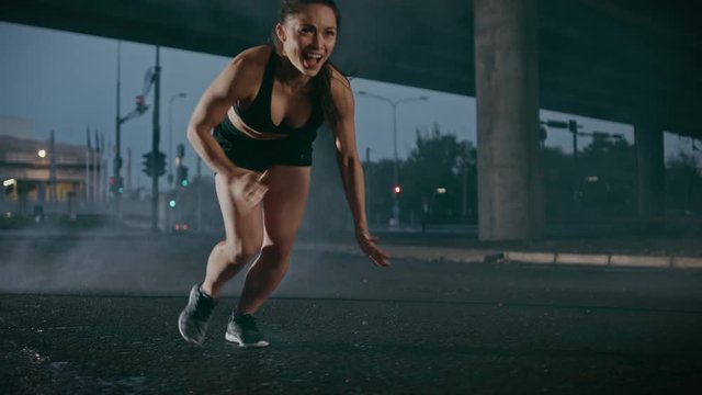Beautiful Fitness Girl in Black Athletic Top and Shorts Starts Sprinting with a Strong Motivational Cry. She is Running in an Urban Environment Under a Bridge with Cars in the Background.