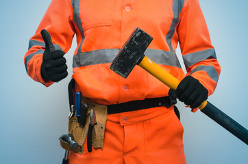 Builder worker holding in hand a big sledgehammer and is showing a thumbs up isolated on blue...