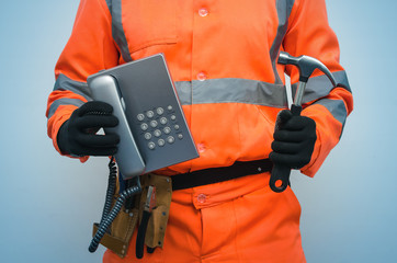 Builder worker is holding in hand a handset phone and hammer. Call to a repair man concept. Contact...