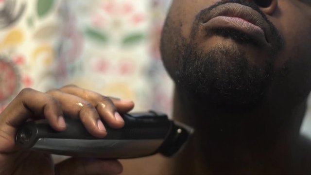 African american black male shaving in the morning to be freshly clean for a good day at work. detail shot shows close up of haired being removed from his face with clippers .