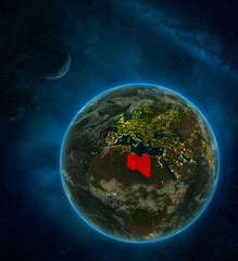 Libya from space on Earth at night surrounded by space with Moon and Milky Way. Detailed planet with city lights and clouds.