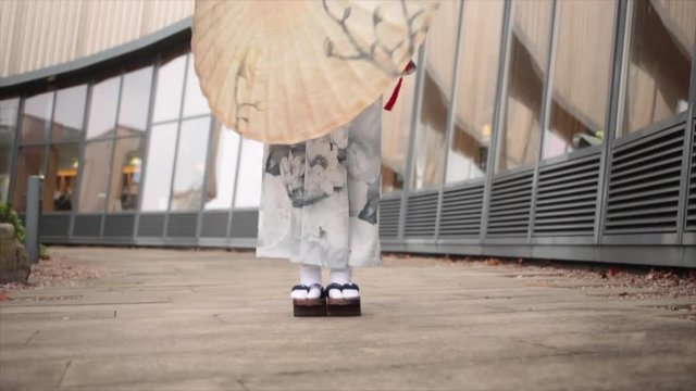 Japanese Geisha wearing wooden geta sandals spins paper umbrella