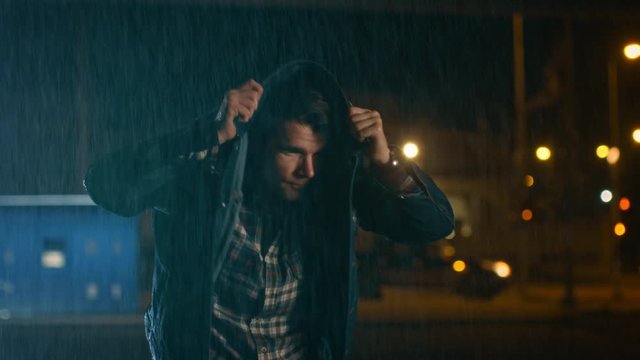 Young Caucasian Man Wearing Square Shirt Using His Jeans Jacket as a Raincoat. Scene is Shot in a City at Night Time and it is Raining.