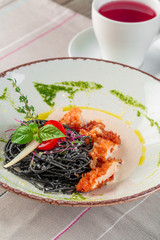 Fresh black tagliolini pasta with chicken in herbs on rucola and tomatoes