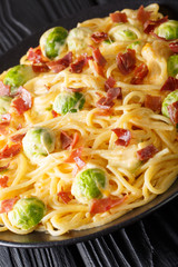 Italian spaghetti with brussels sprouts and ham with cheese sauce close-up on a plate. vertical
