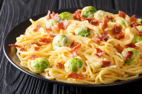 Italian pasta cooked with Brussels sprouts, ham covered with creamy cheese sauce close-up on a plate. horizontal