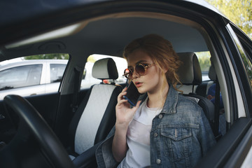 Beautiful girl sits behind the wheel of a premium car, looks the way and talking on the phone.