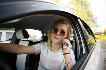 Beautiful girl sits behind the wheel of a premium car, looks the way and talking on the phone.