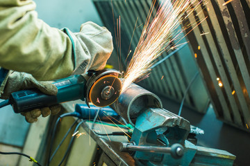 mechanic cleans a welded seam on a section of a steel pipe with the help of a grinding machine in...