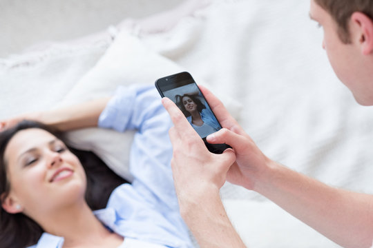 man taking photos of woman lying in bed. hobby and mobile photography concept.