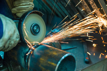 mechanic cleans a welded seam on a section of a steel pipe with the help of a grinding machine in the metal workshop - obrazy, fototapety, plakaty