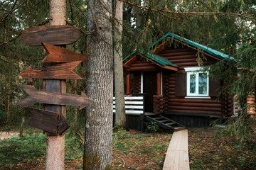 Wooden arrow pointers on the tree. Wooden house in the forest in the background. Selective focus on...