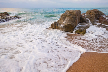 Beautiful seashore landscape with sea foam and rocks at sunrise
