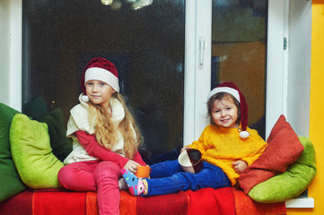 Fototapeta premium Pretty little girl in Christmas hats Santa in the house in anticipation of Christmas