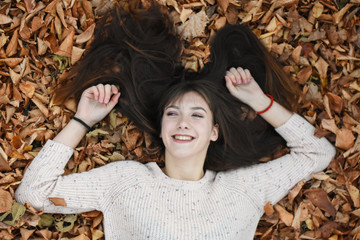 Beautiful teenage girl lying in the leaves. Young woman in autumn leaves