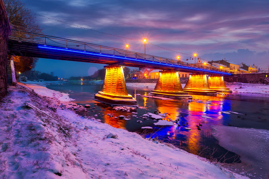 beautiful evening cityscape of old european town Uzhgorod in winter. wonderful cloudy sky over the river Uzh with some ice and snow on the shore. citylights reflect on the water surface