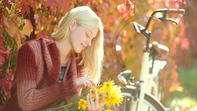 Woman with yellow flovers. Autumn happy girl and joy. Dreamy girl with long hair in knit sweater. Autumn woman with retro bike with flowers in basket in autumnal park. Clouse up portrait of girl.