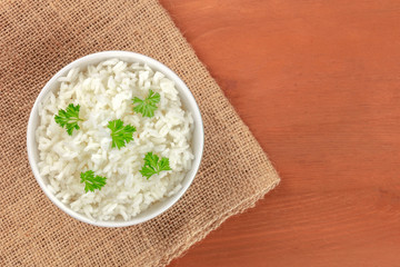 A photo of a bowl of cooked white long rice, shot from the top on rustic textures with copy space