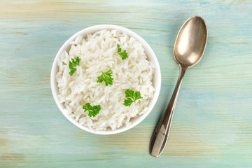 A photo of a bowl of cooked white long rice, shot from the top on a teal blue background with a spoon and copy space