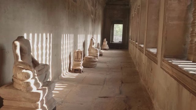 Forward Dolly Inside A Hallway With Headless Statues And Light Shining From The Windows, Inside Angkor Wat.