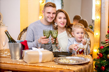 Happy young family, father, mother and son, in Christmas evening in home. They sitting at the table at Christmas dinner. New Year's and Christmas theme. Holiday mood