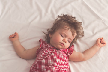 Baby girl sleeping on back with open arms and without pacifier in a bed with white sheets. Peaceful...