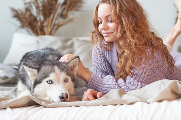 woman in a cozy knitted sweater relaxes on the bed. her dog is near. best friends concept