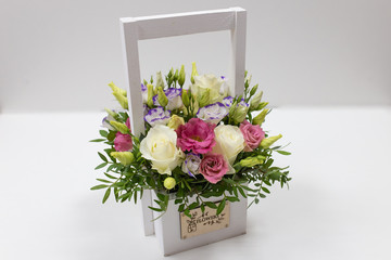 Bright floral arrangement of roses in a light wooden box with a handle on a light background.