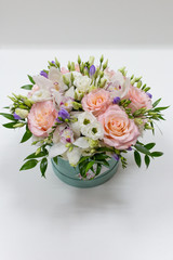 Delicate bouquet of white and pink roses and orchids with green leaves in a hat box of cerulean color on a light background