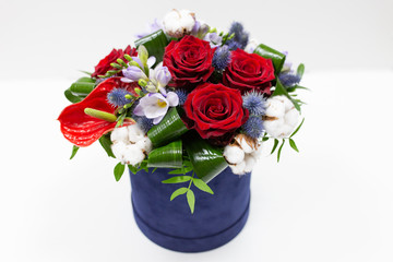 A bright bouquet of red flowers (rose and anthurium) with green leaves, Alstroemeria and cotton flowers in a blue box for hats on a light background