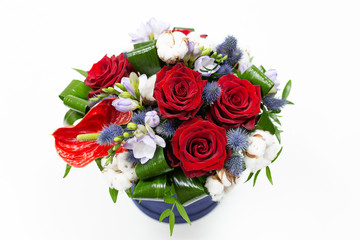 A bright bouquet of red flowers (rose and anthurium) with green leaves, Alstroemeria and cotton flowers in a blue box for hats on a light background