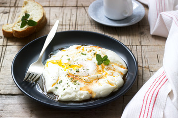 Cilbir, poached egg in yogurt with spiced butter and herbs, served with bread and a cup of coffee.