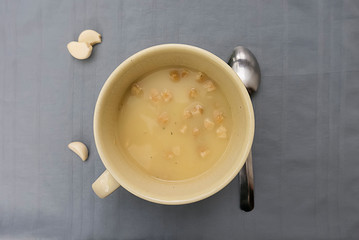 Chicken cream soup with croutons in a yellow cup on a gray background.
