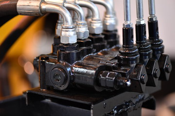 Partial view of a hydraulic system. Four shiny metal-hoses in a black distributor.