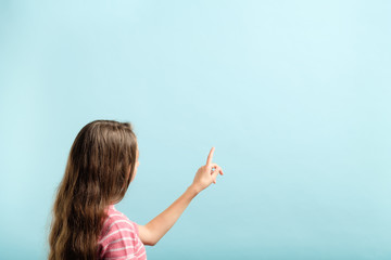 girl using index finger to press invisible button on blue background. interface or virtual screen...
