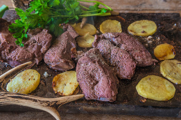 Hunting season meal: deer meat roasted with potatoes, parsleay on the plate close up