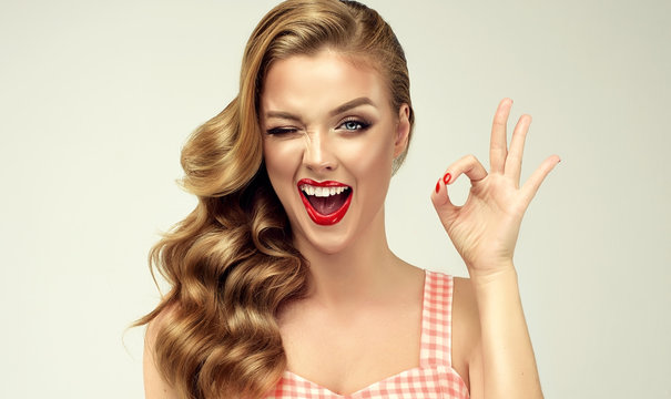 Pin-up retro girl with curly hair  winking, smiling and showing OK sign . Presenting your product. Expressive facial expressions
