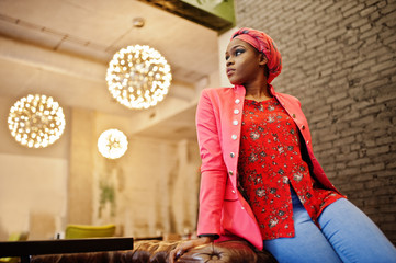 Stylish african woman in red shirt, jacket and hat posed indoor cafe.