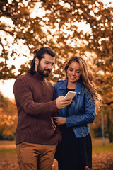 Young couple using cellphone in autumn colored park.