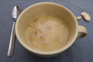 Chicken cream soup with croutons in a yellow cup on a gray background.