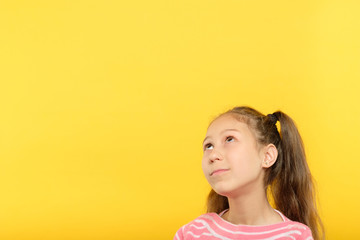 cute little girl looking up on virtual object or text on yellow background. empty space for advertisement.