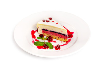 Plate with sweet layered cheesecake dessert decorated with mint and strawberry jam cream isolated at white background.