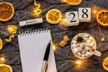 Winter composition. Wooden calendar January 28th Cup of cocoa with marshmallow, empty open notepad...
