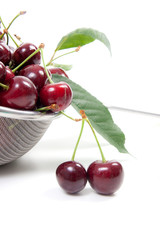 Steel colander with red sweet cherry isolated on a white background..