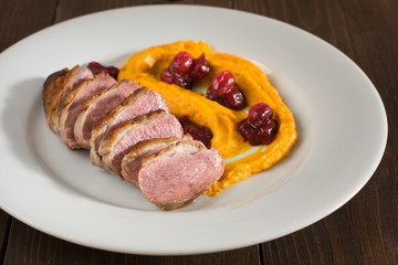 closeup of a duck breasts with squash puree and cranberries