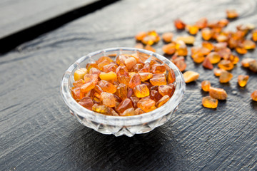 Cute little bowl cup full of small Baltic amber chips on dark brown wooden background. The Baltic region is home to the largest known deposit of amber, called Baltic amber or succinite.