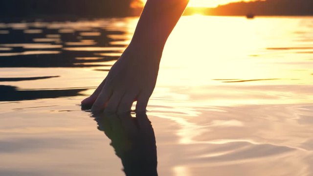 Hand Gently Touches The Surface Of The Water In The Golden Sunset