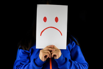 Depression. A woman in a blue sweater holding and covering and hiding  her face with a white...