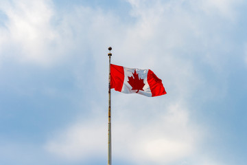 Canadian flag with the traditional maple leaf waving in the blue sky of Toronto, Quebec, Canada